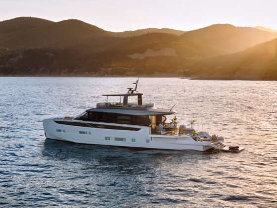 Luxury catamaran-style yacht on calm sea at sunset, with hills in the background and people dining on the deck.