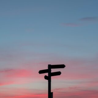 Silhouette of a multi-arrow signpost against a pink and blue sunset sky with clouds.