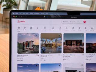 Airbnb homepage on a laptop screen showing a search bar and category icons (Desert, Beach, Cabins, Islands).