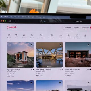 Airbnb homepage on a laptop screen showing a search bar and category icons (Desert, Beach, Cabins, Islands).