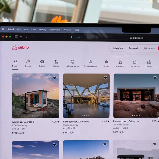 Airbnb homepage on a laptop screen showing a search bar and category icons (Desert, Beach, Cabins, Islands).
