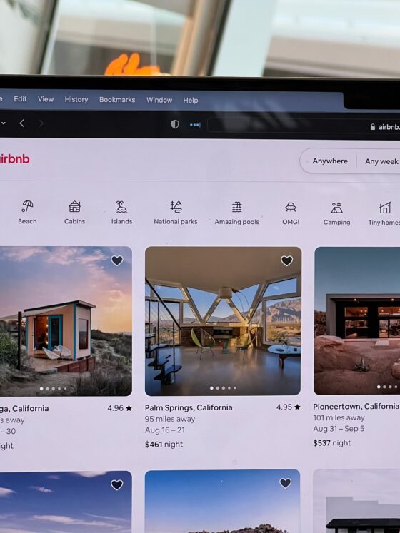 Airbnb homepage on a laptop screen showing a search bar and category icons (Desert, Beach, Cabins, Islands).