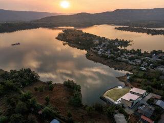 Aerial view of a calm lake at sunset, with a small peninsula town along the shore and a modern villa by the water.