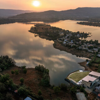 Aerial view of a calm lake at sunset, with a small peninsula town along the shore and a modern villa by the water.