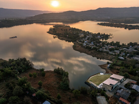 Aerial view of a calm lake at sunset, with a small peninsula town along the shore and a modern villa by the water.