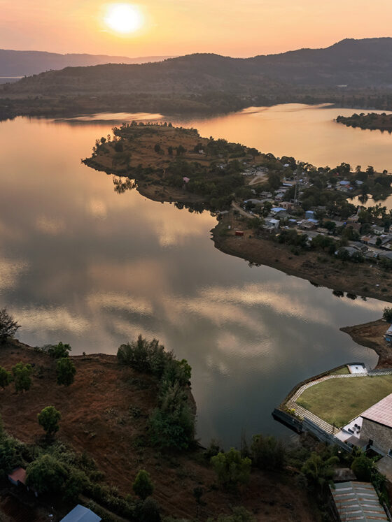 Aerial view of a calm lake at sunset, with a small peninsula town along the shore and a modern villa by the water.